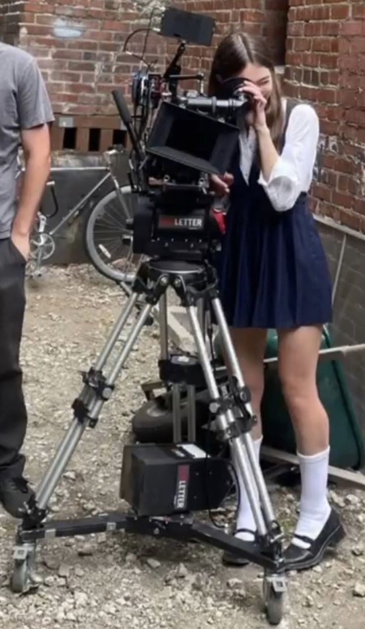 a man standing next to a woman in front of a camera on a tripod