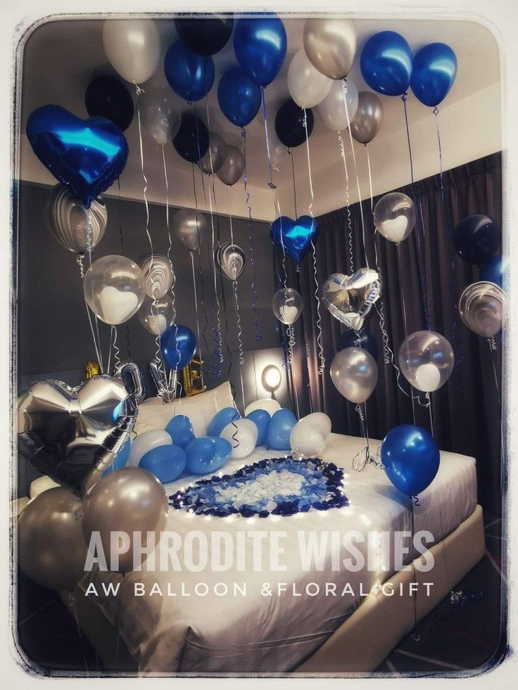 blue and white balloons are hanging from the ceiling above a bed in a room with black curtains