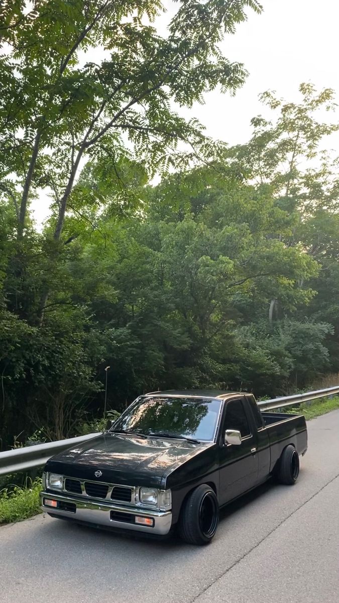 a black pickup truck parked on the side of a road next to trees and bushes