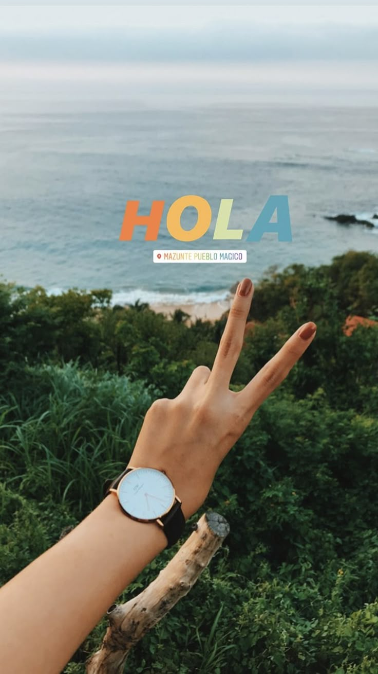 a person's hand holding up the word hola in front of an ocean