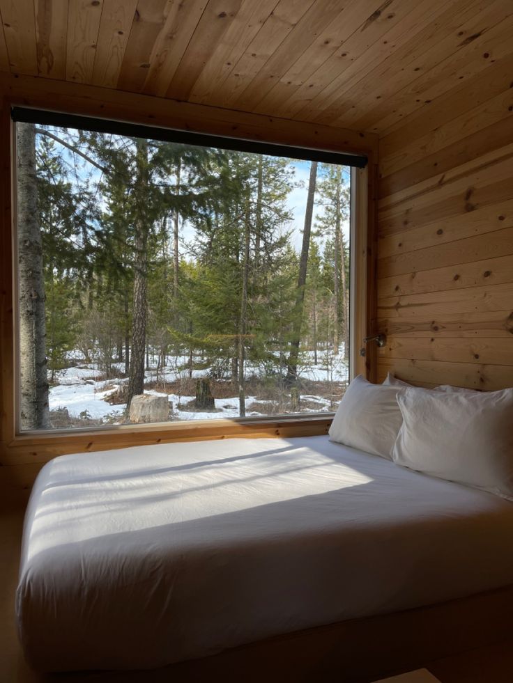 a bed in a bedroom next to a window with snow on the ground and trees outside