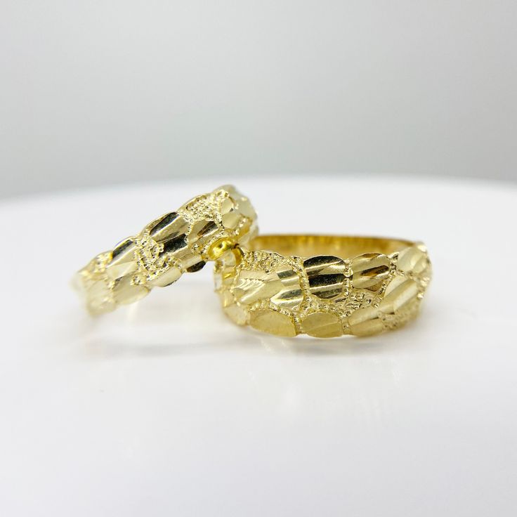 two gold wedding rings sitting side by side on a white surface, with one ring in the middle