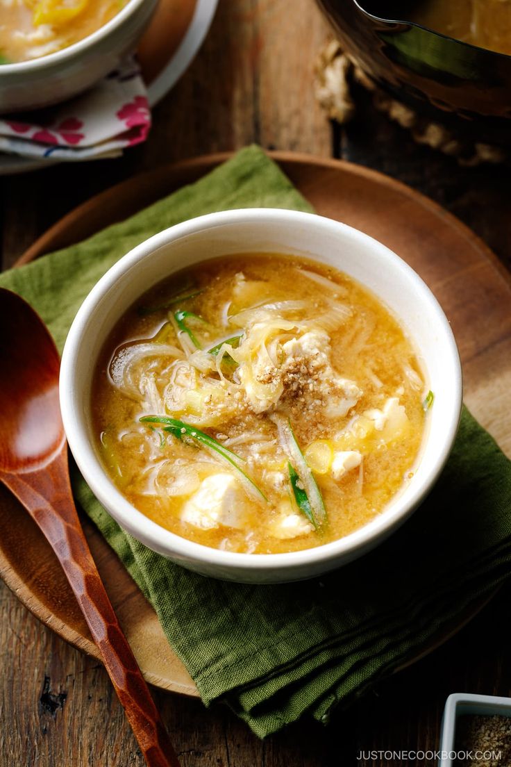 a bowl of soup on top of a wooden table next to a plate with spoons