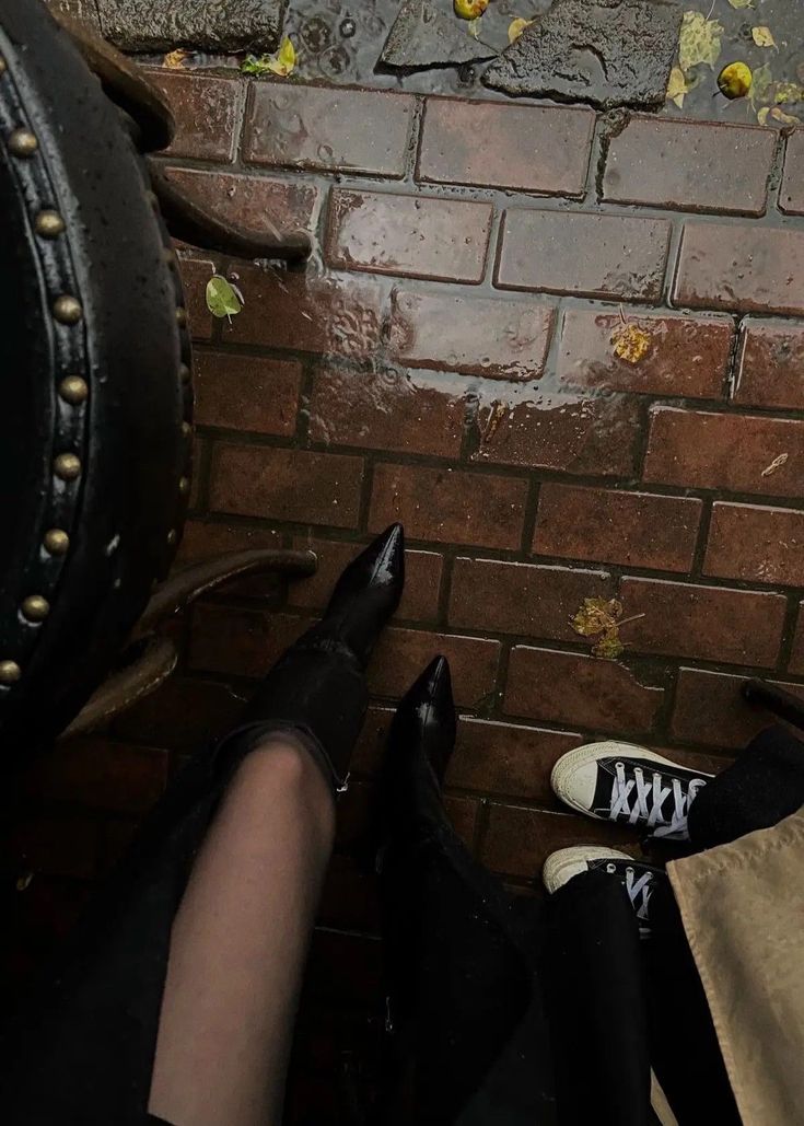 a person standing next to a brick wall with their feet up on the ground and wearing black shoes