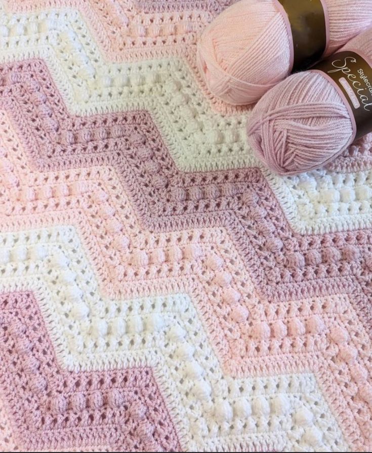 two balls of yarn sitting on top of a pink and white crocheted blanket