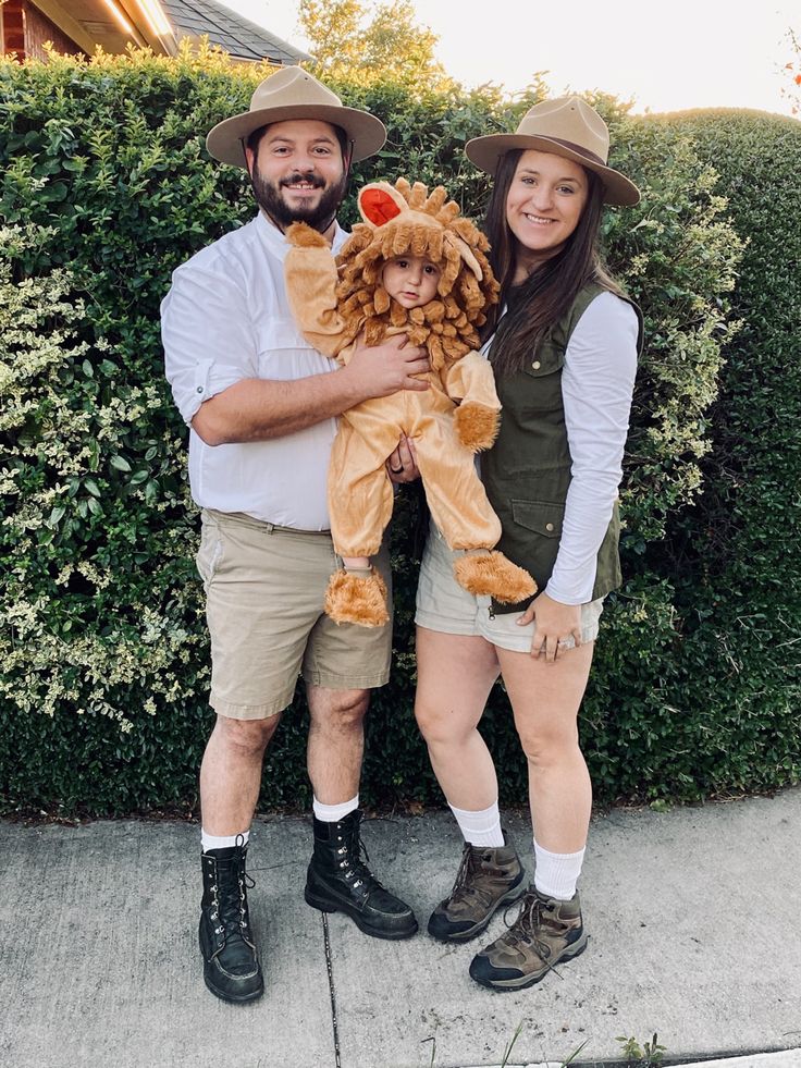 a man and woman standing next to each other holding a stuffed animal in front of a hedge