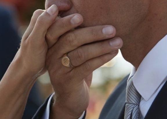 a close up of a person wearing a suit and tie holding his hand to his face