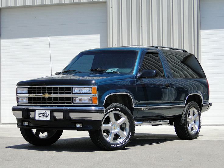 a blue truck is parked in front of a building with two garage doors behind it