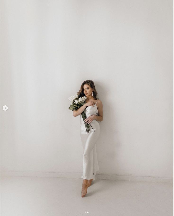 a woman in white is holding flowers and posing for the camera with her arms behind her back