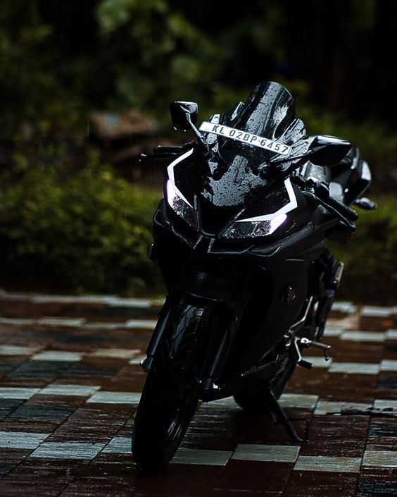 a black motorcycle parked on top of a checkered tile floor in front of trees