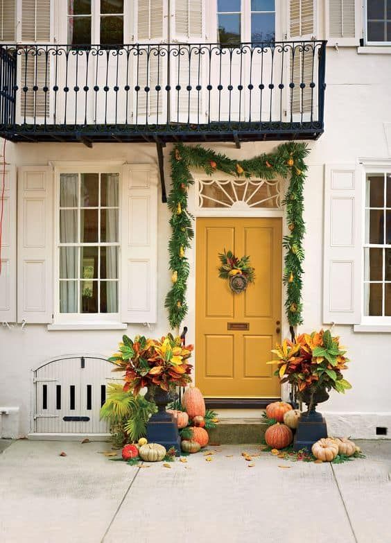 a yellow door is surrounded by pumpkins and greenery in front of a white house