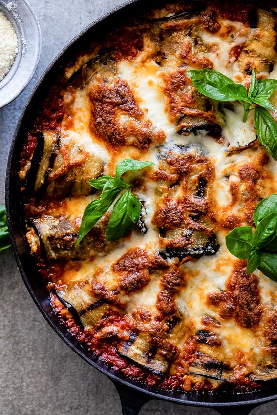 a skillet filled with meat and cheese covered in basil leaves on top of a table