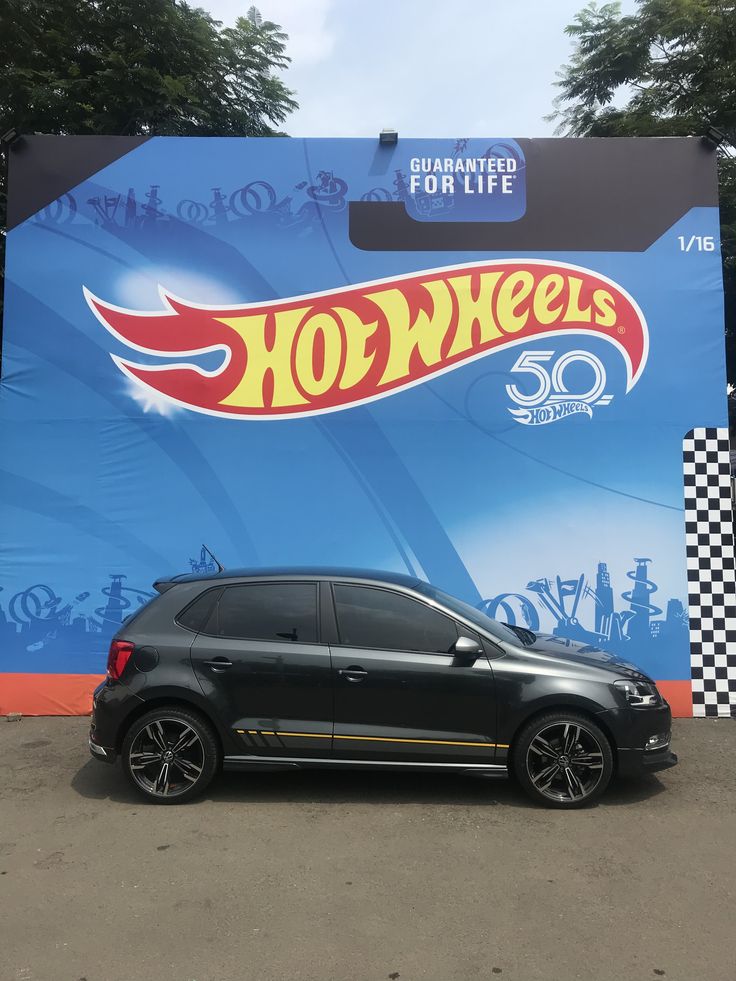 a small black car parked in front of a large advertisement for the hot wheels movie