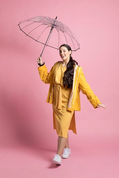 a woman is holding an umbrella and smiling at the camera while standing against a pink background