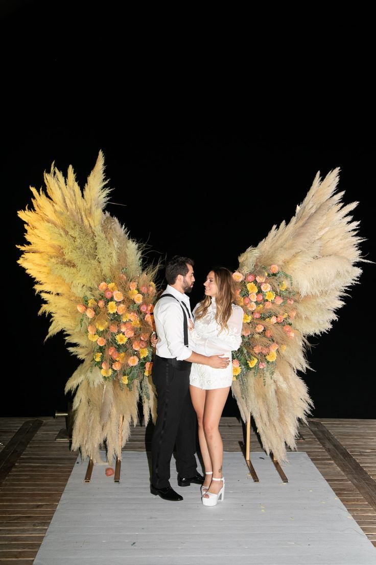 a man and woman standing next to each other on a wooden platform with tall grass