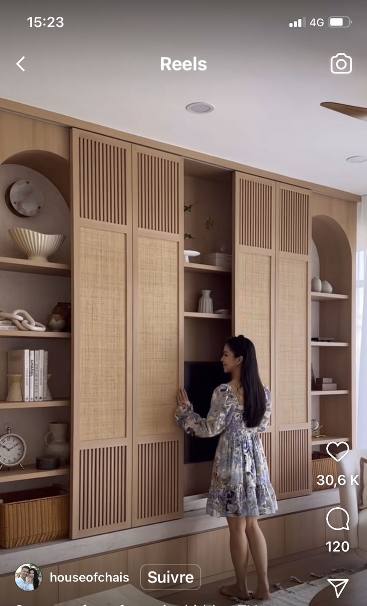 a woman standing in front of a wall unit with shelves and cupboards on it