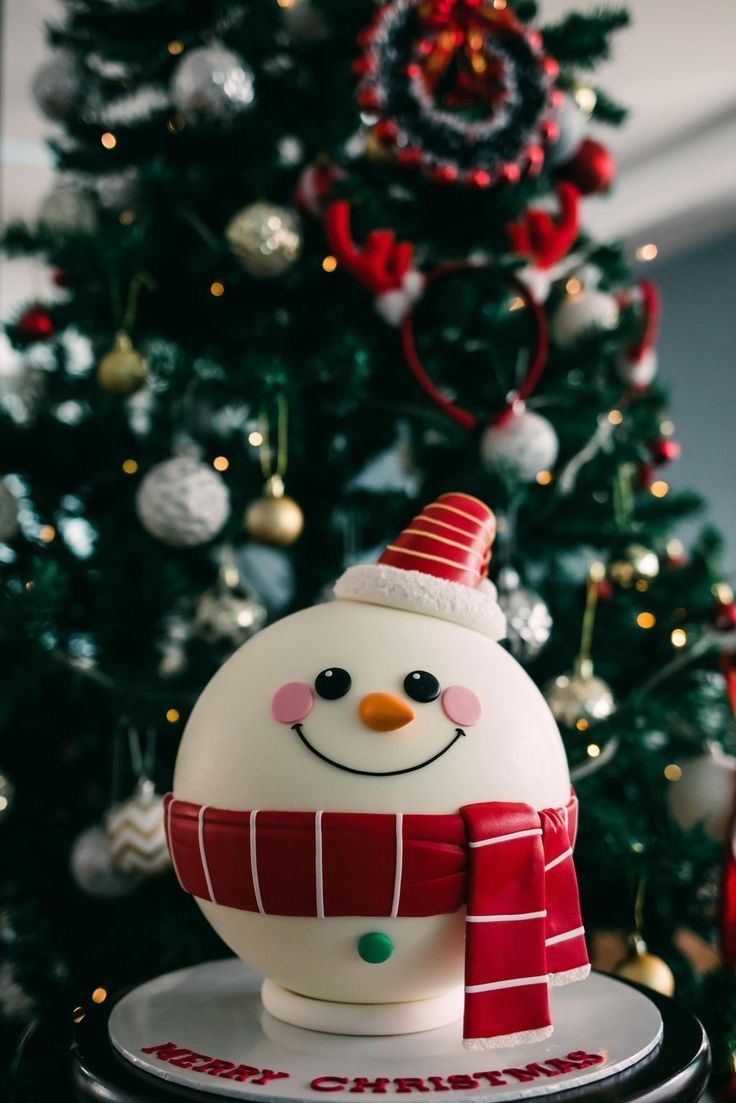 a snowman cake sitting in front of a christmas tree