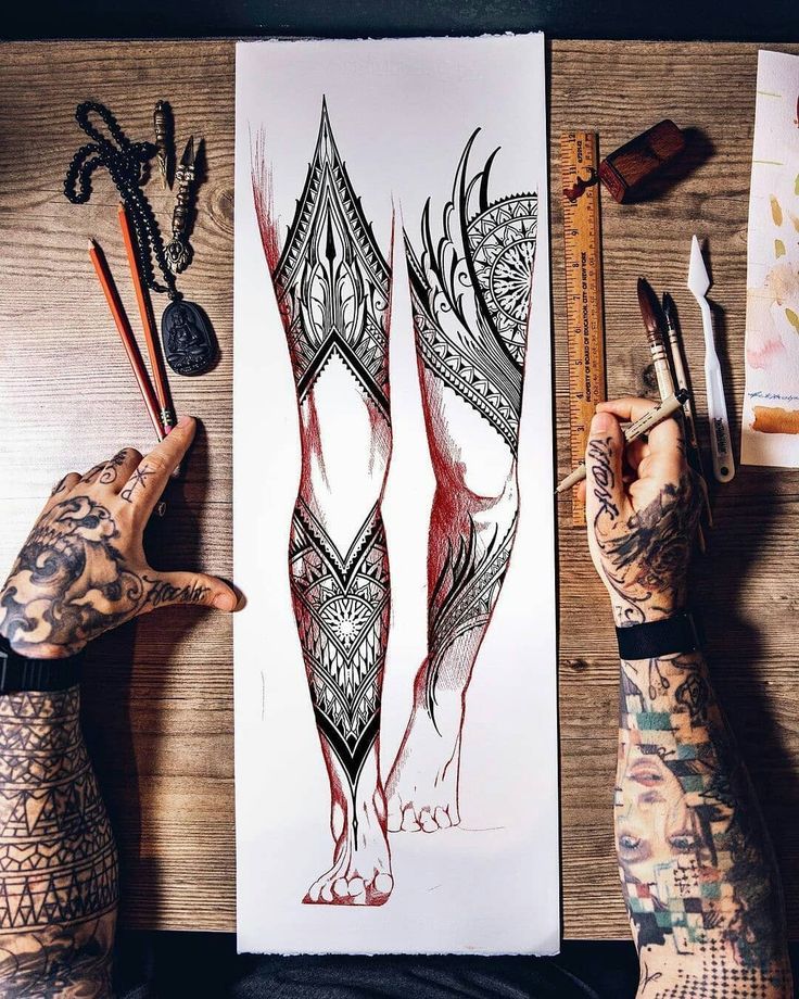 two tattooed hands holding scissors next to a piece of art on a wooden table with other items