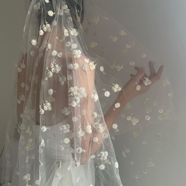 a woman wearing a veil with white flowers on it and her hands in the air