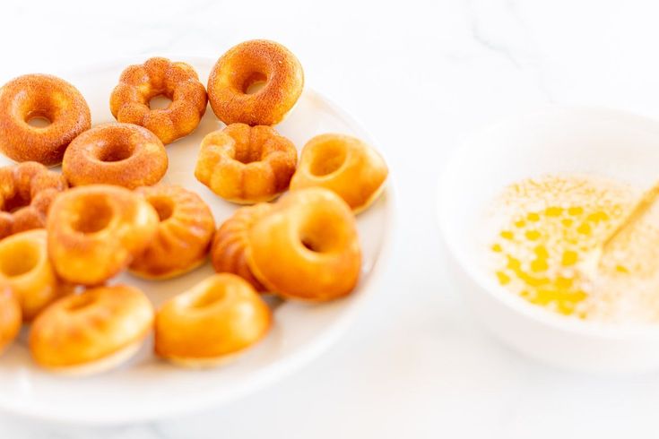 there are many donuts on the plate next to a bowl of mustard and a spoon