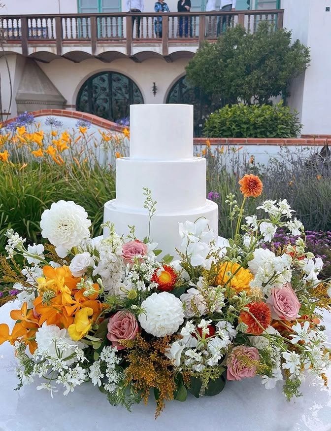 a three tiered white wedding cake sitting on top of a table covered in flowers