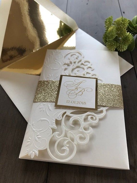 a white and gold wedding card on top of a wooden table next to a flower