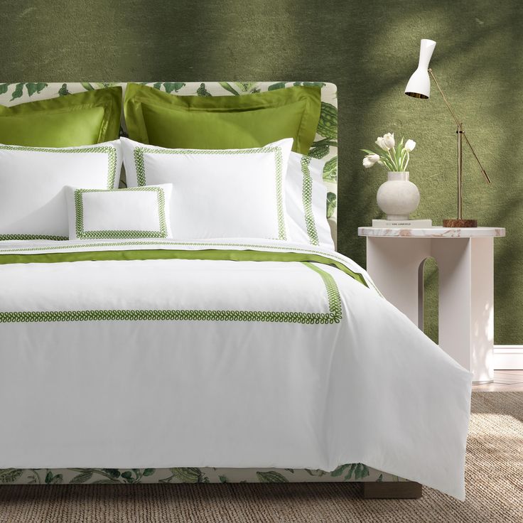 a bed with green and white comforters in a room next to a lamp on a table