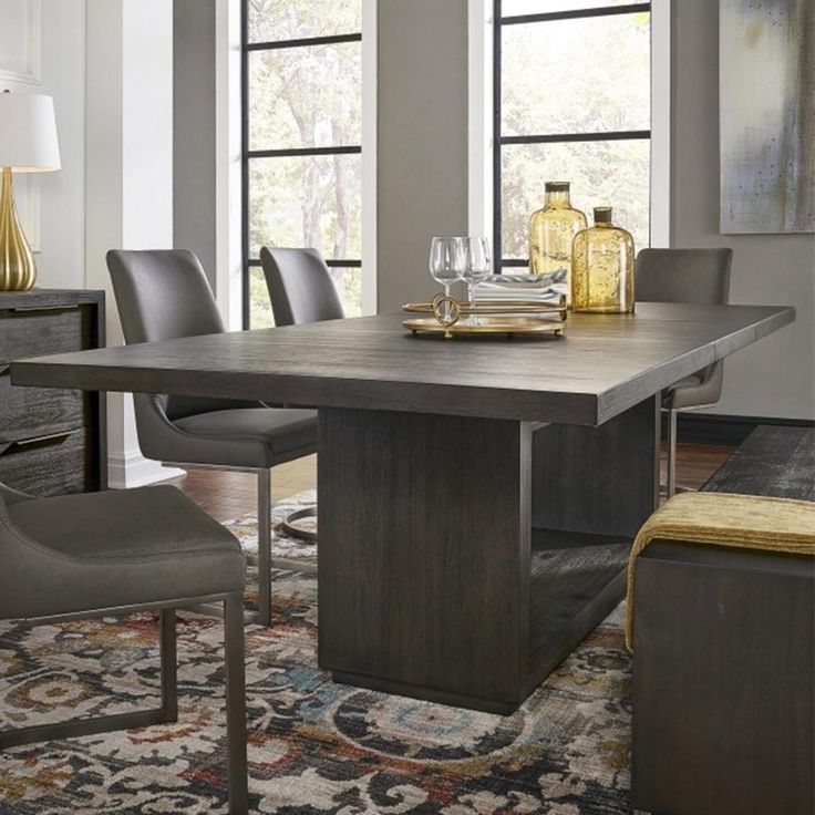 a dining room table with chairs and an area rug in front of the window that has a painting on it