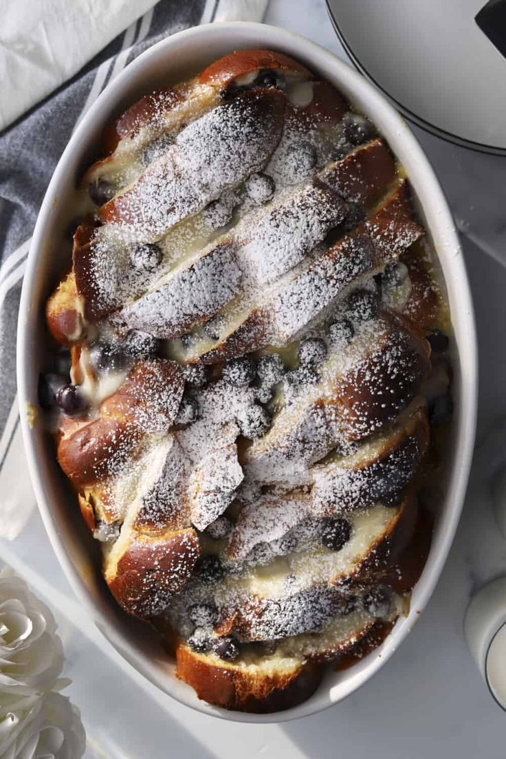 a white dish filled with bread covered in powdered sugar on top of a table