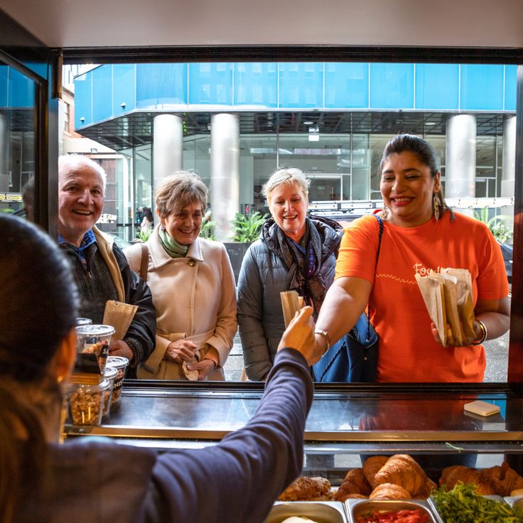 a group of people standing at a counter with food in front of them and one person handing something to the other