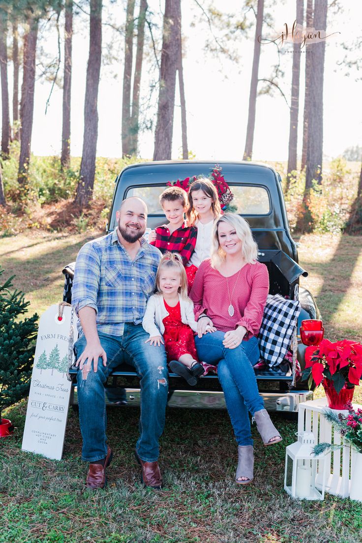 a family sitting in the back of a pickup truck with christmas trees and presents on the bed