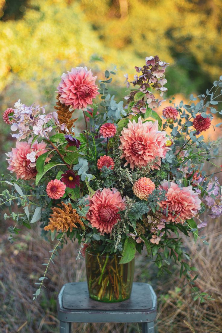 a vase filled with lots of flowers sitting on top of a wooden chair in the grass