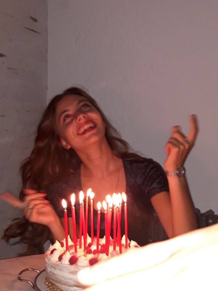 a woman sitting in front of a cake with lit candles on it and pointing to the side