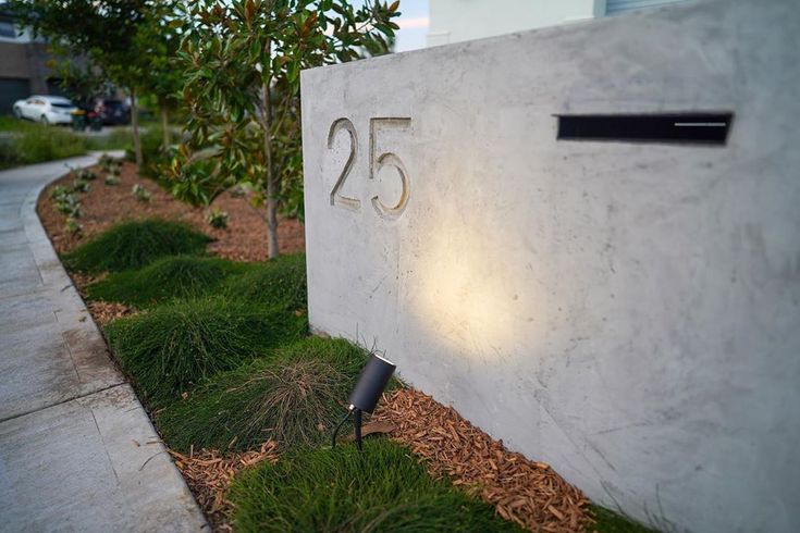 a house number sign with grass growing in the front and sidewalk behind it on a sunny day