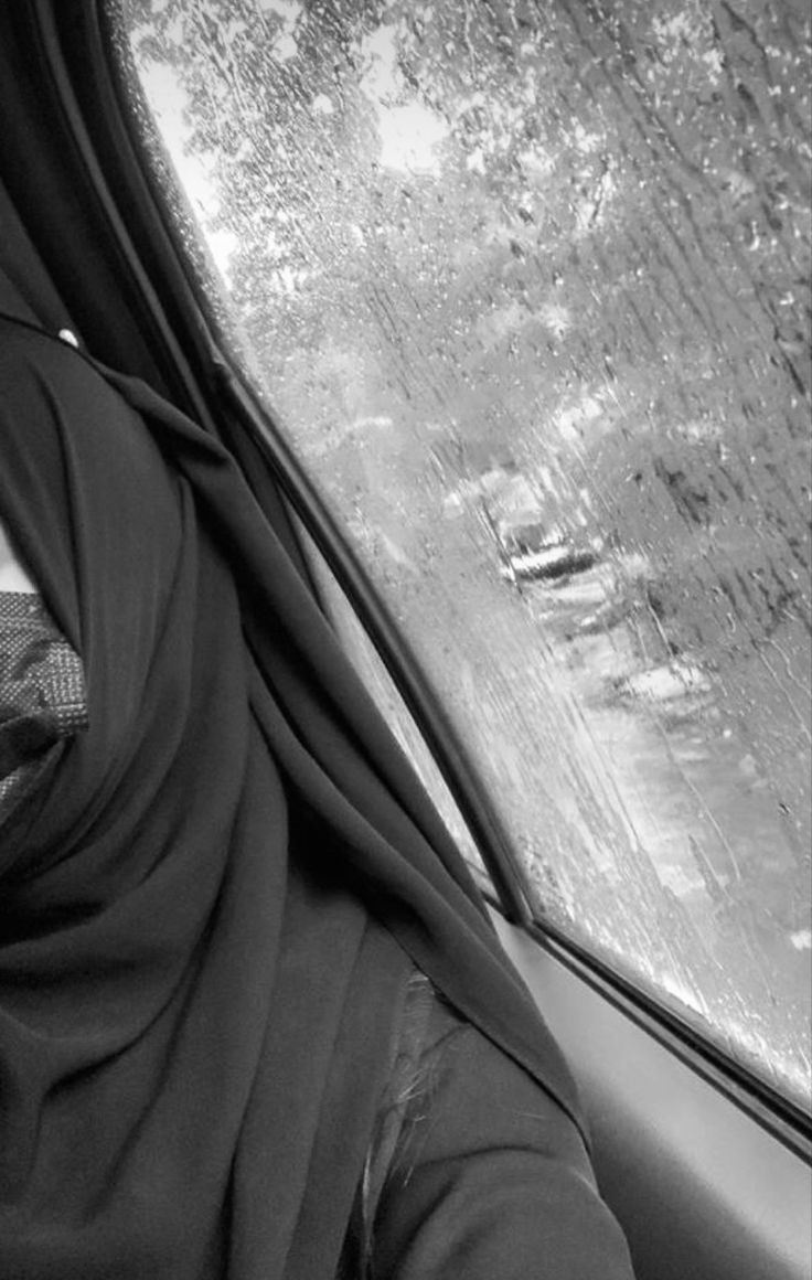 a woman sitting in the passenger seat of a car wearing a hijab and looking out the window