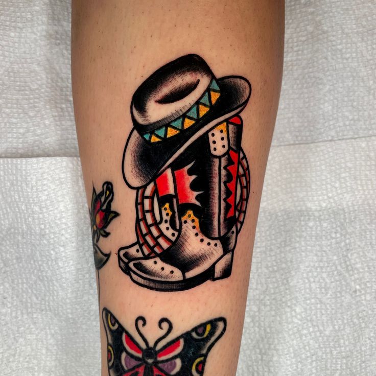 a tattoo on the leg of a person wearing boots and a hat with butterflies around it