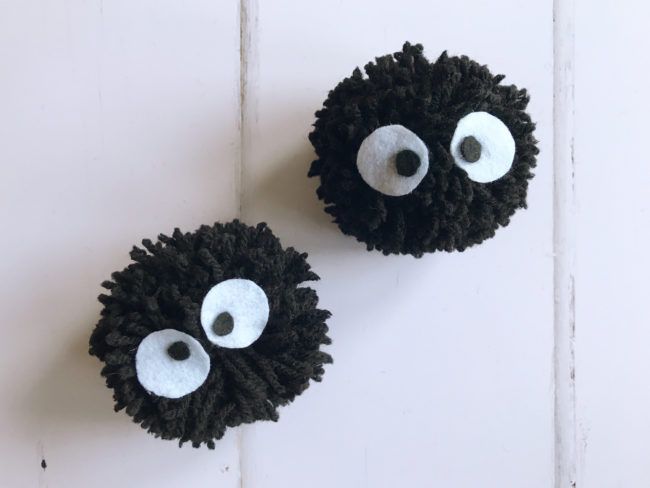 two black and white balls with googly eyes hanging on the wall, one is made out of yarn