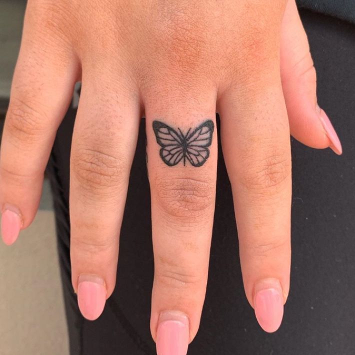 a woman's hand with a small butterfly tattoo on her left ring finger and pink nail polish