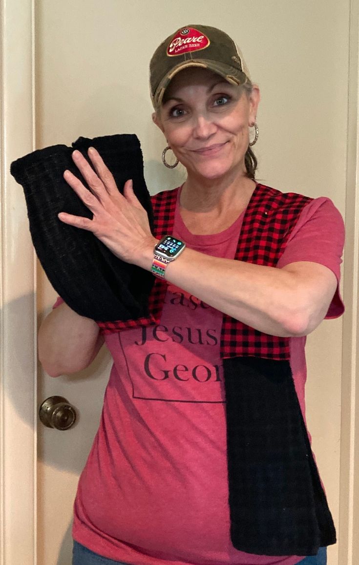 a woman wearing a pink shirt and hat holding up a black towel in front of a door