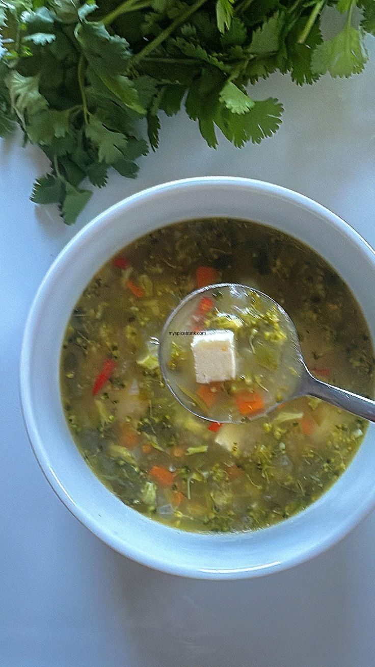 a white bowl filled with soup next to a bunch of parsley on top of a table