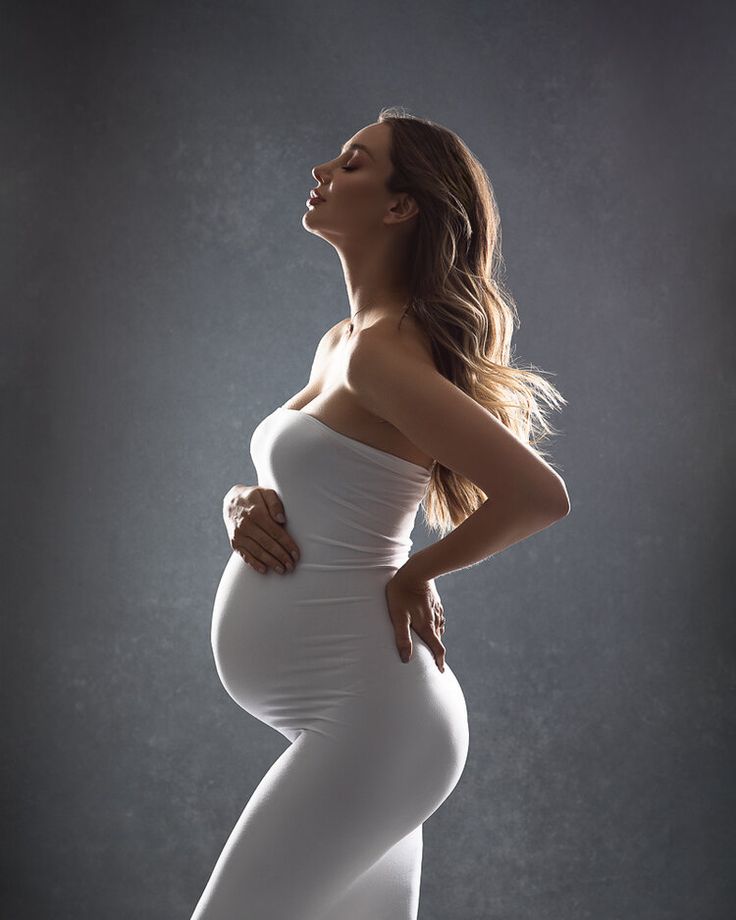 a pregnant woman in white dress posing for the camera with her hands on her hips