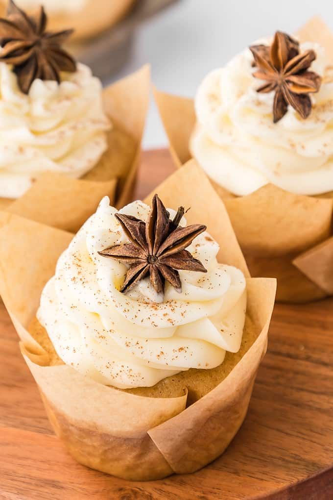 three cupcakes with cinnamon star anise on top are sitting on a wooden plate