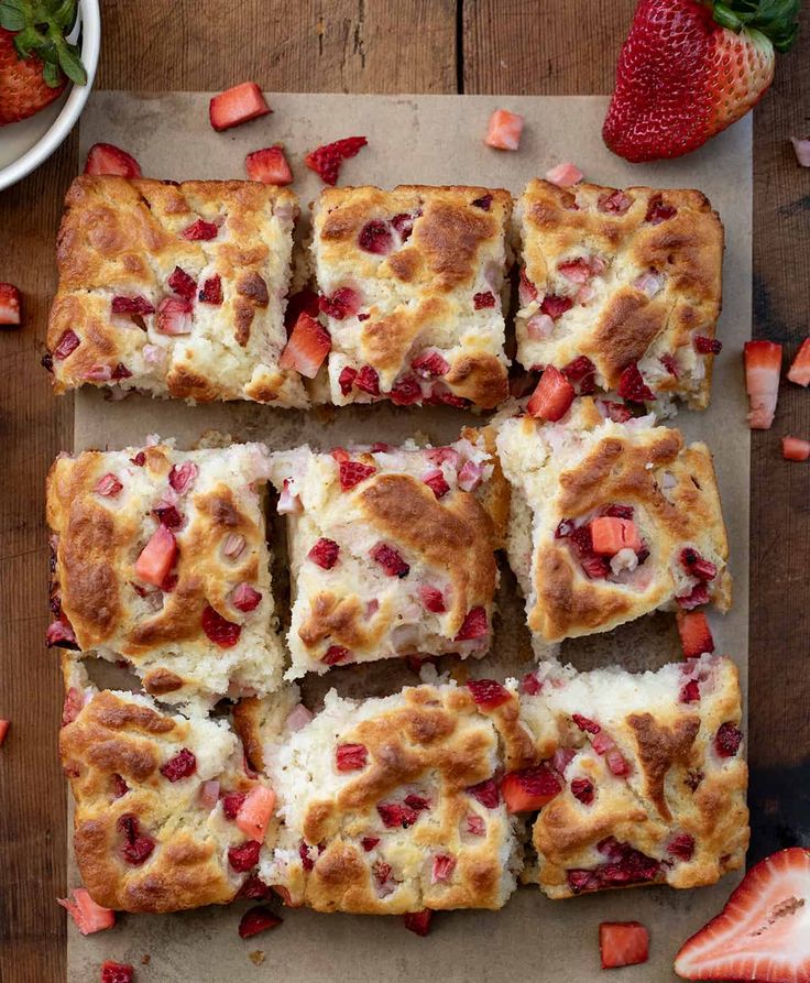 strawberry shortcakes cut into squares on a cutting board with strawberries around them