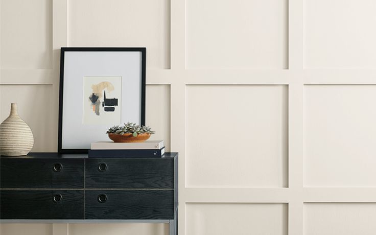 a black dresser with a white vase sitting on top of it next to a wall