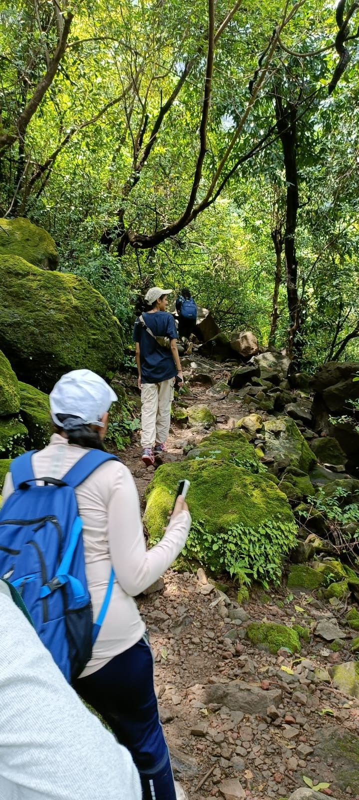 two people walking up a trail in the woods with backpacks and cell phones on their backs