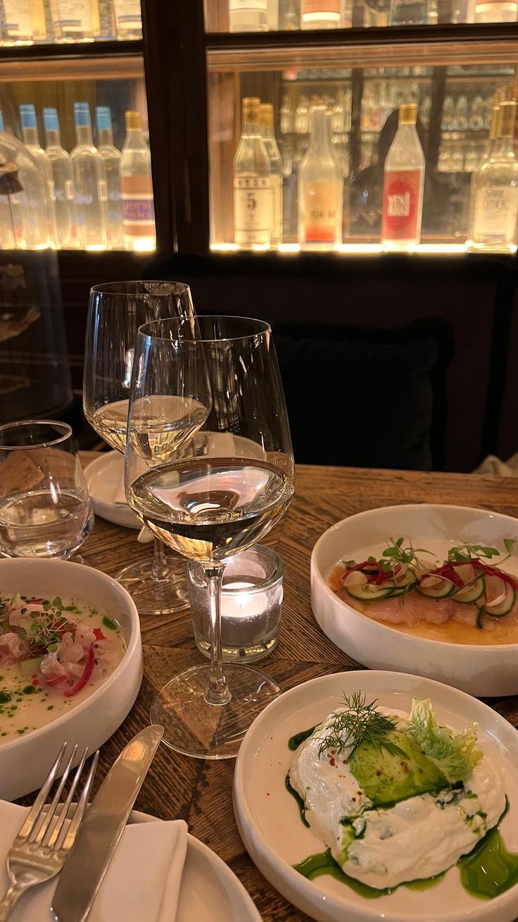 a table topped with plates and bowls filled with food next to wine glasses on top of a wooden table