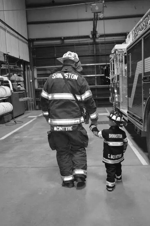 two firemen walking towards a firetruck in a warehouse with hoses attached to it