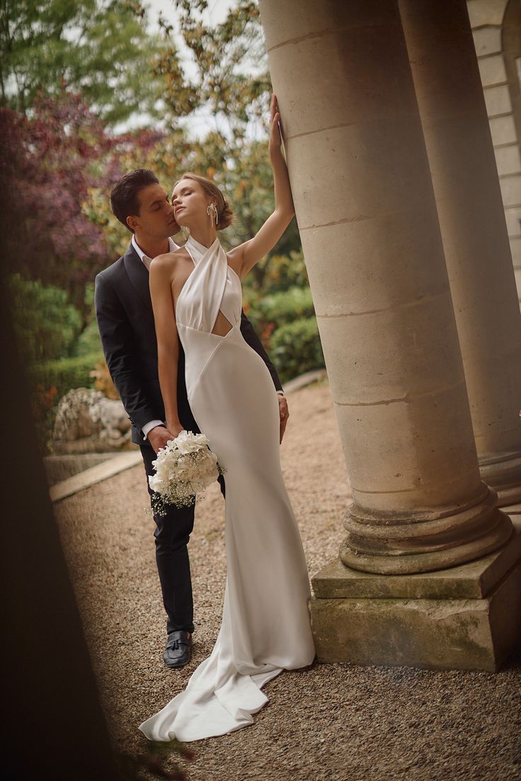 a bride and groom standing next to each other in front of pillars with flowers on them