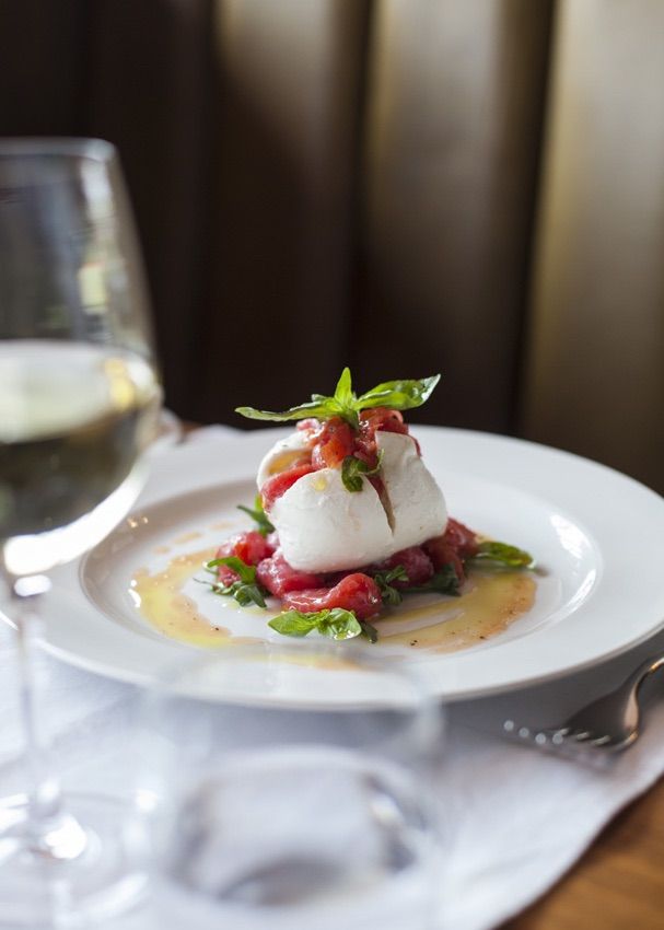 a white plate topped with food next to a glass of wine on top of a table