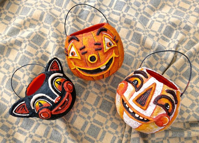 three pumpkins with faces painted on them sitting next to each other in front of a patterned cloth